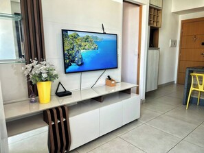 A modern living room with a flat-screen TV mounted on a white cabinet, a small wooden side table, and a yellow vase with white flowers. - 2802 Unique · Studio Unique with garage (Sacramenta)
