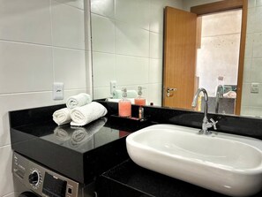 A bathroom with a black countertop, a white sink, and a mirror. There are towels and toiletries on the counter. - 2802 Unique · Studio Unique with garage (Sacramenta)