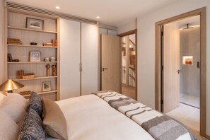 A bedroom with a bed, a bedside table, a lamp, a wardrobe, and a shelf with books and decorative items. - Cadogan Street IV by onefinestay (London)