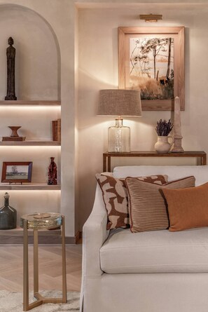 A well-lit living room with a sofa, decorative pillows, a lamp, a painting, and a statue on a shelf. - Cadogan Street IV by onefinestay (London)