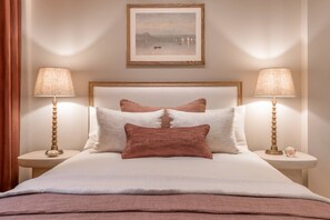 Cama bem arrumada com cabeceira, duas luminárias de cabeceira e um quadro emoldurado acima.