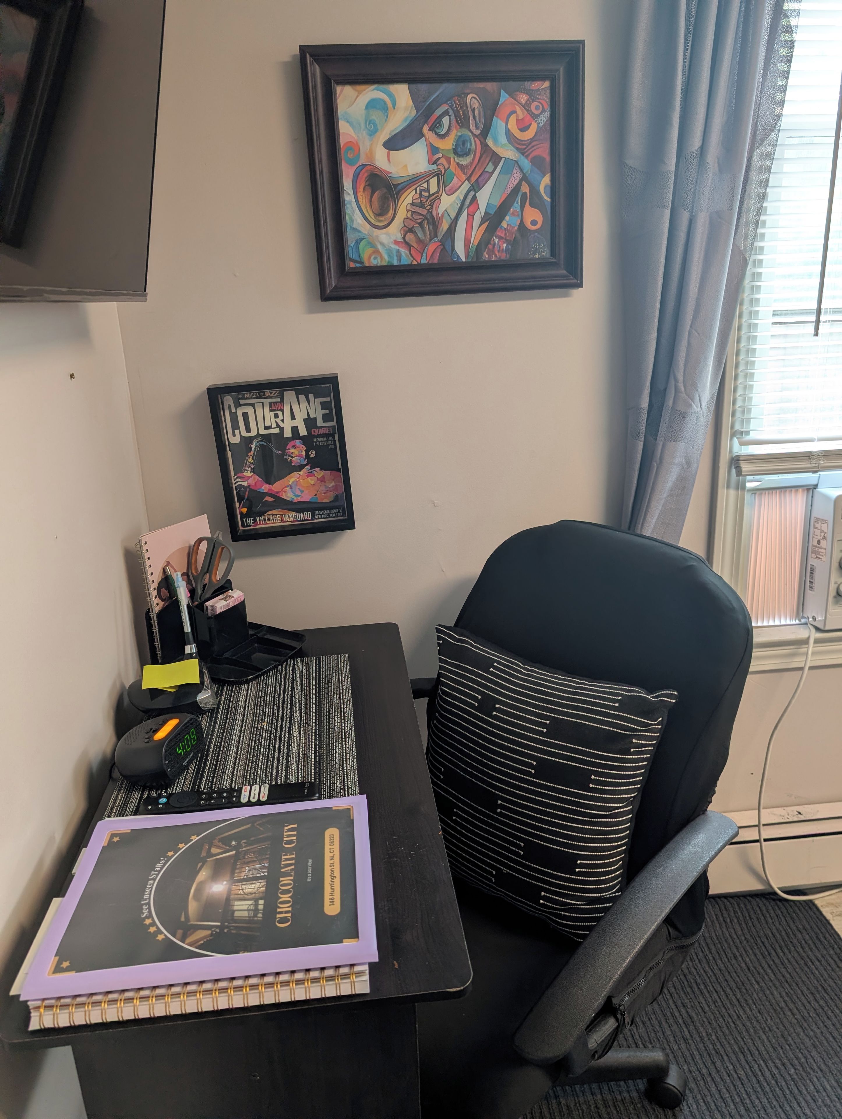 Ein Schreibtisch mit einem Notizbuch, einer Uhr und einem gerahmten Bild an der Wand.