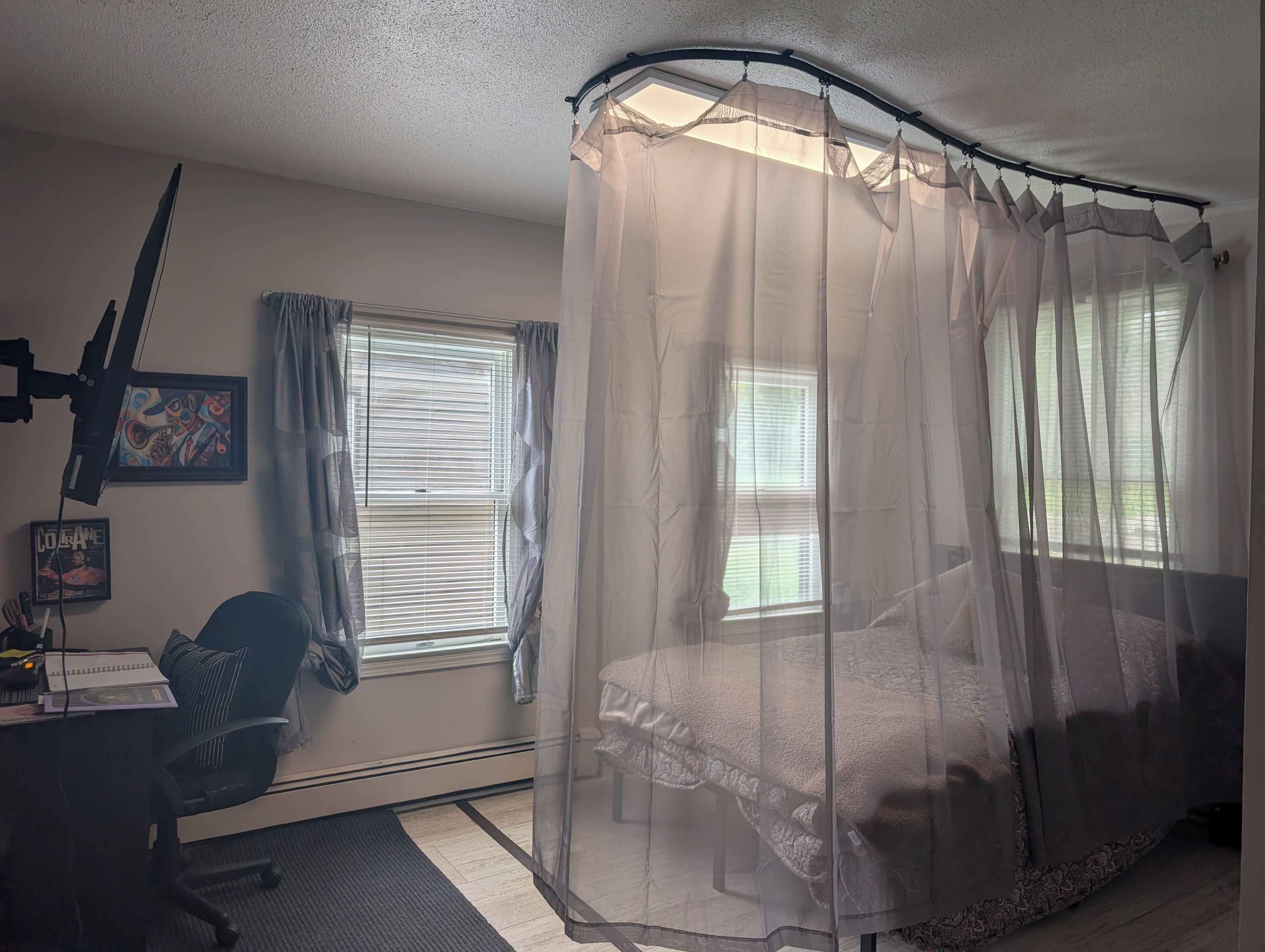A bedroom with a bed, a desk with a chair, a window with blinds, and a ceiling fan.