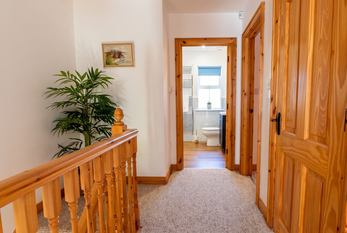 A hallway with a wooden railing, a potted plant, and a door leading to a bathroom.