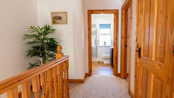 A hallway with a wooden railing, a potted plant, and a door leading to a bathroom.