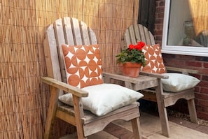 Two wooden chairs with white cushions and orange patterned backrests, placed on a wooden table with a potted plant.