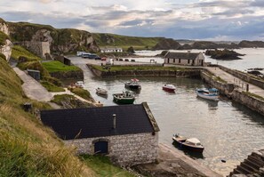 A coastal harbor with boats, a stone building, and a grassy hillside. - 3-Bed Family House Sleeps 6 · Fireplace & Garden · Walk to Portstewart Golf Club (Co Londonberry)