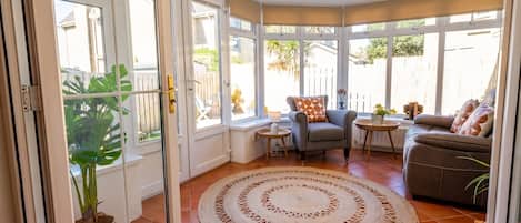A sunlit room with a large window, a round woven rug, and a grey sofa.