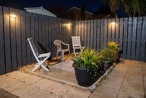 Een terras met twee witte stoelen, een zwarte plantenbak met planten en een houten omheining.