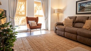 Ein Wohnzimmer mit einem braunen Sofa, einem braunen Sessel, einer Stehlampe und einem großen Fenster mit Vorhängen.