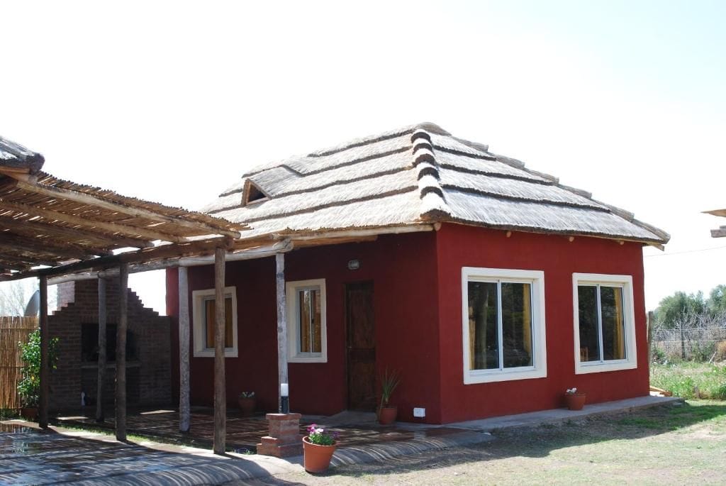 Un bâtiment rouge avec un toit de chaume, une véranda et des plantes en pot.