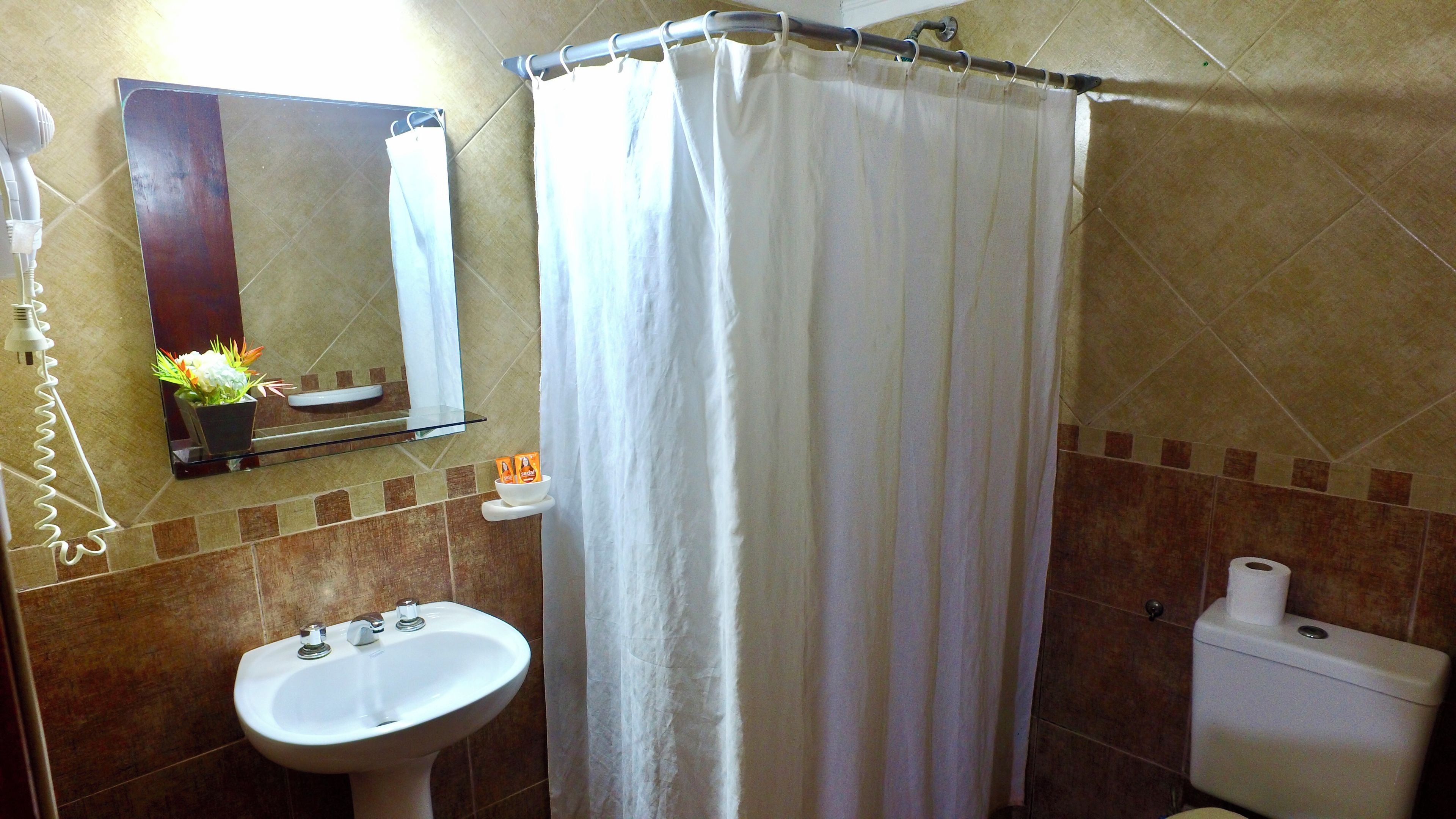 Un baño con lavamanos, inodoro, cortina de ducha y espejo.