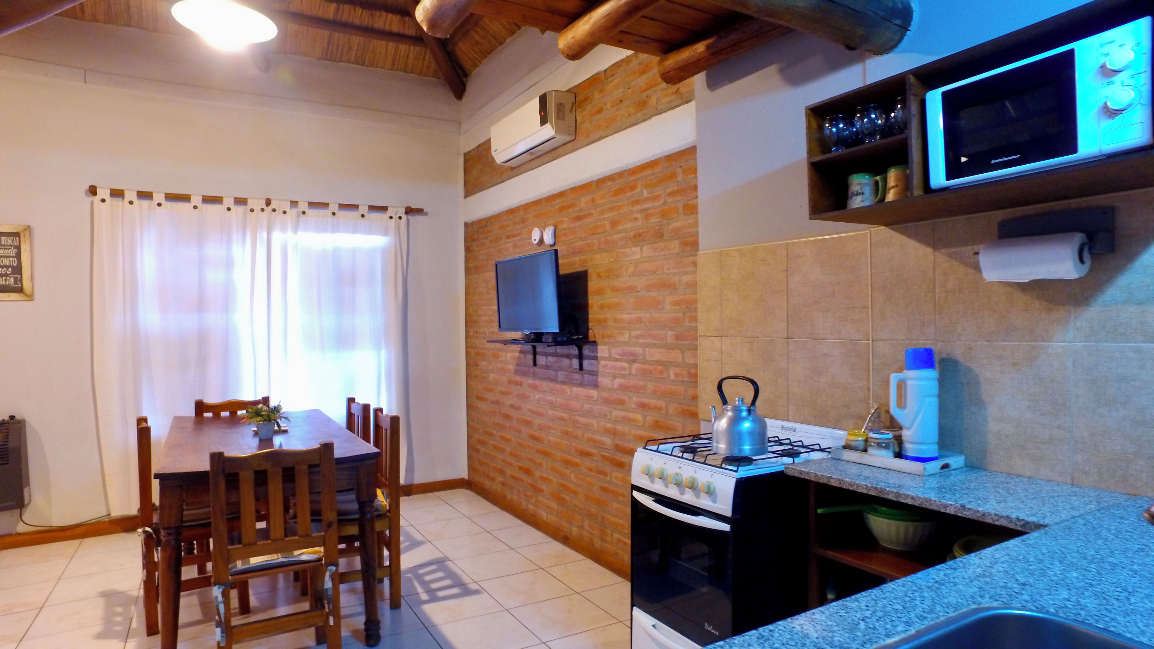 Una cocina compacta con estufa a gas, microondas y televisor montado en la pared.