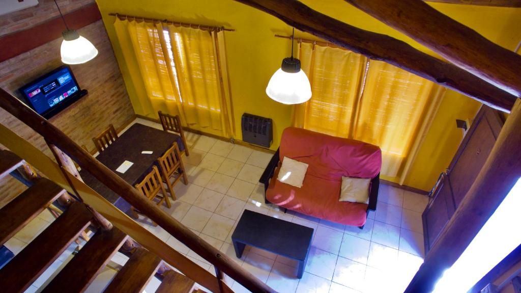 A room with a red sofa, wooden dining table, chairs, a television, and yellow curtains.