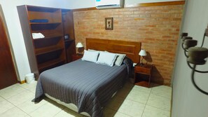 Un dormitorio con cama, dos mesitas de noche, un armario de madera y una pared de ladrillo.