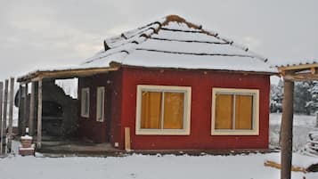 Un pequeño edificio rojo con techo nevado y dos ventanas con cortinas amarillas.