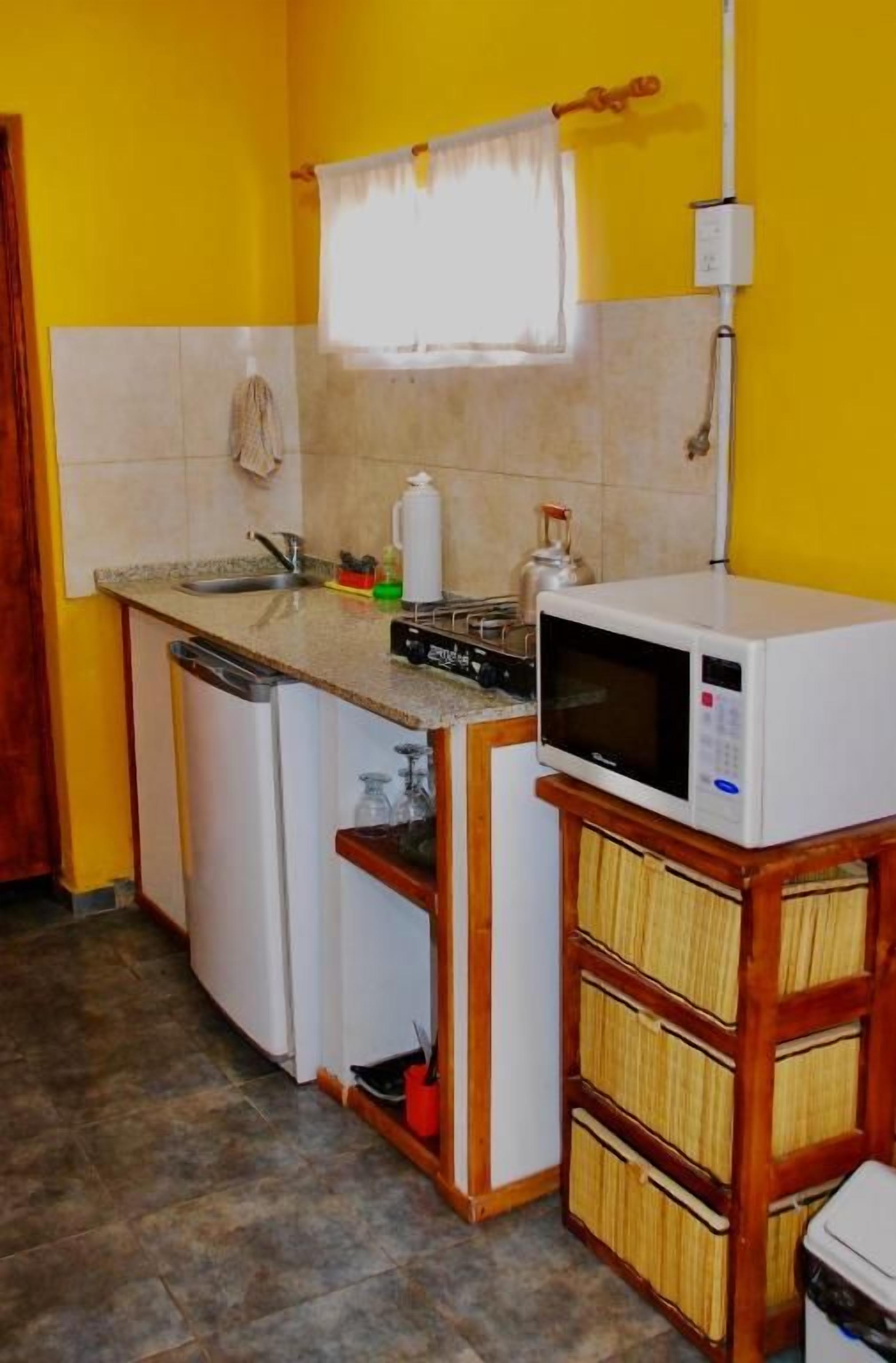 Una cocina compacta con microondas, un refrigerador pequeño y un lavamanos.