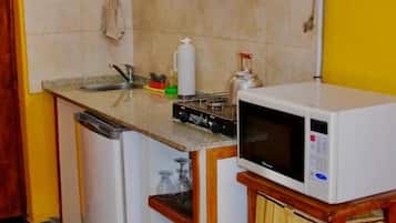 Una cocina compacta con microondas, un refrigerador pequeño y un lavamanos.