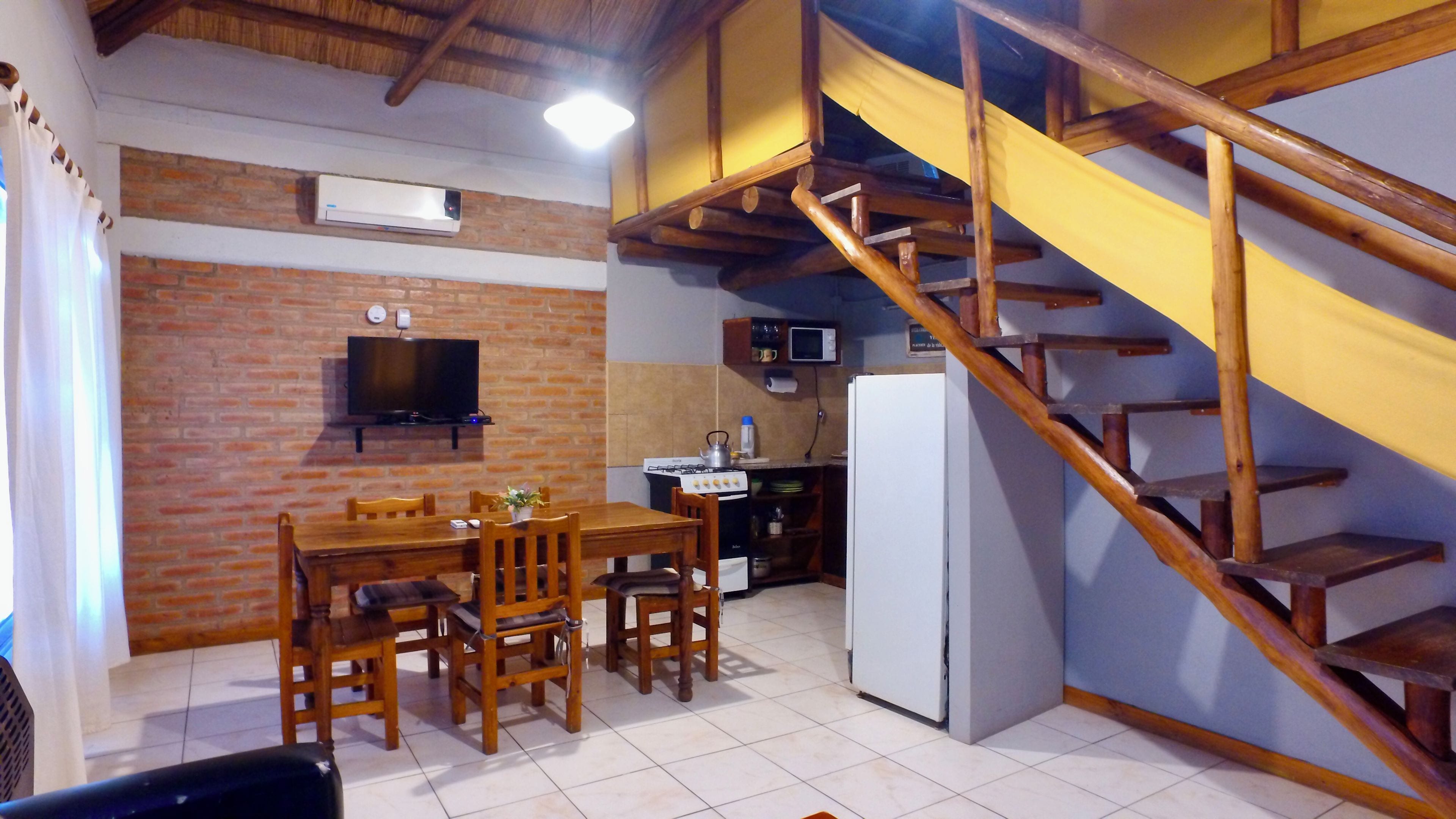 Un comedor con pared de ladrillo, televisor y cocina equipada con estufa y refrigerador.