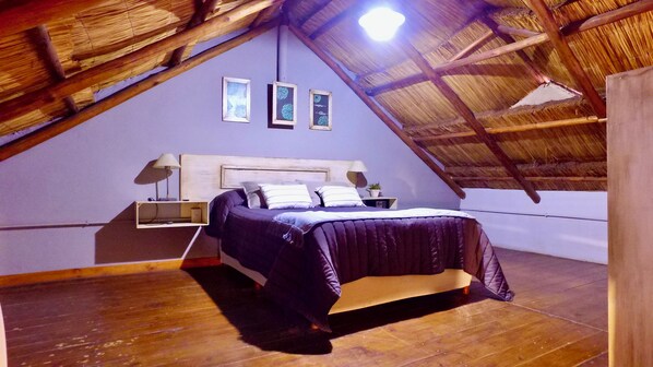 Un dormitorio con techo inclinado, una cama, mesitas de noche y cuadros en la pared.