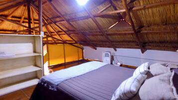 A room with a bed, a shelf, and a thatched roof.
