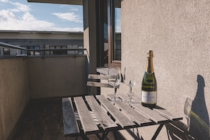 Ein Balkon mit einem Holztisch, einer Weinflasche und zwei Gläsern.