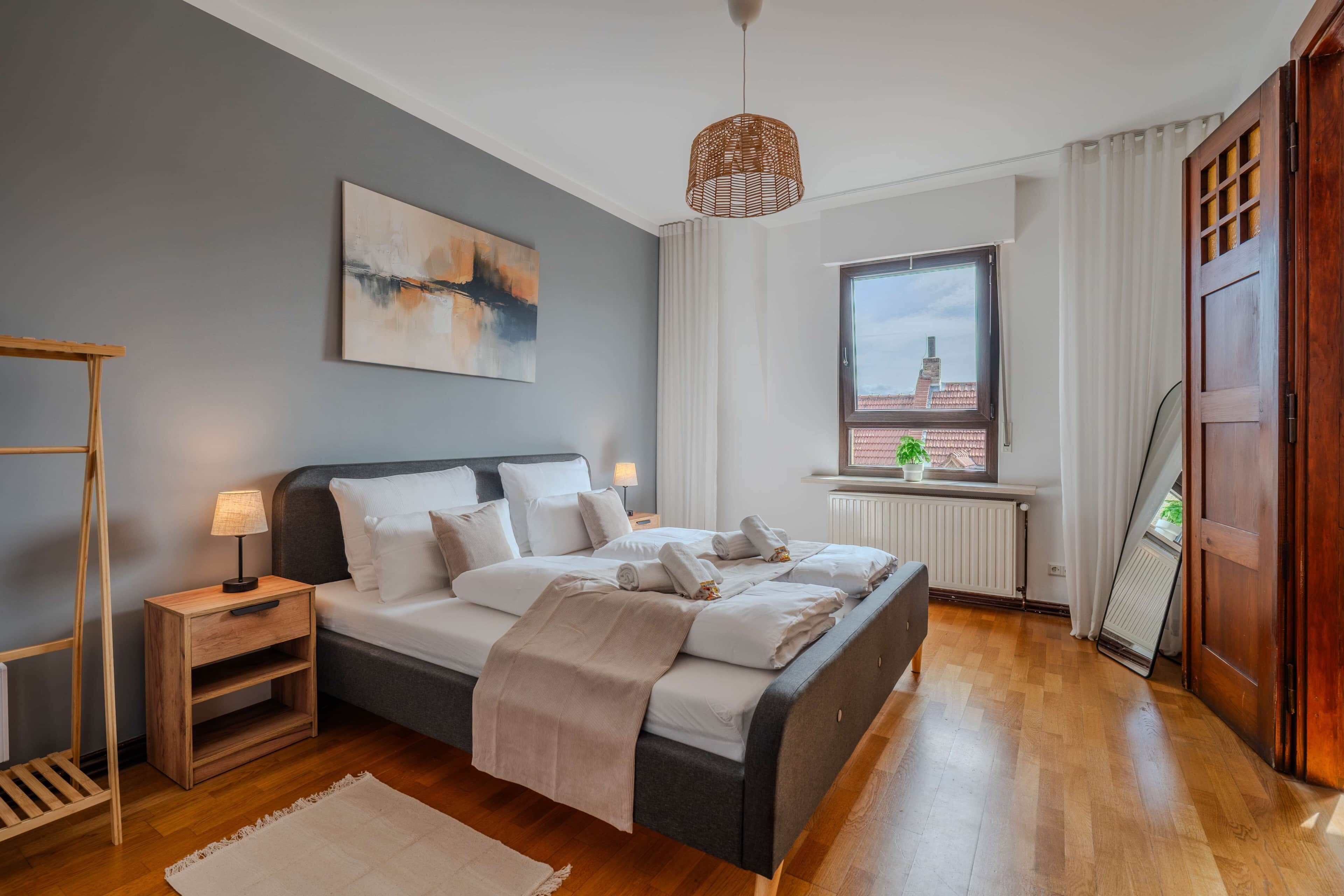 A modern bedroom with a bed, bedside tables, a hanging light fixture, a window with a view, and a radiator.