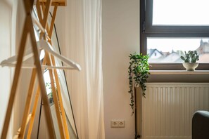 A room with a radiator, a window with a view of buildings, and a plant on the windowsill.