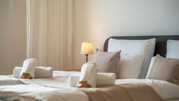 Una cama bien hecha con almohadas y una toalla enrollada, una lámpara de noche y una ventana con cortinas.