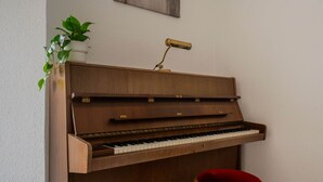 Ein stehendes Holzklavier mit einem roten Hocker davor.