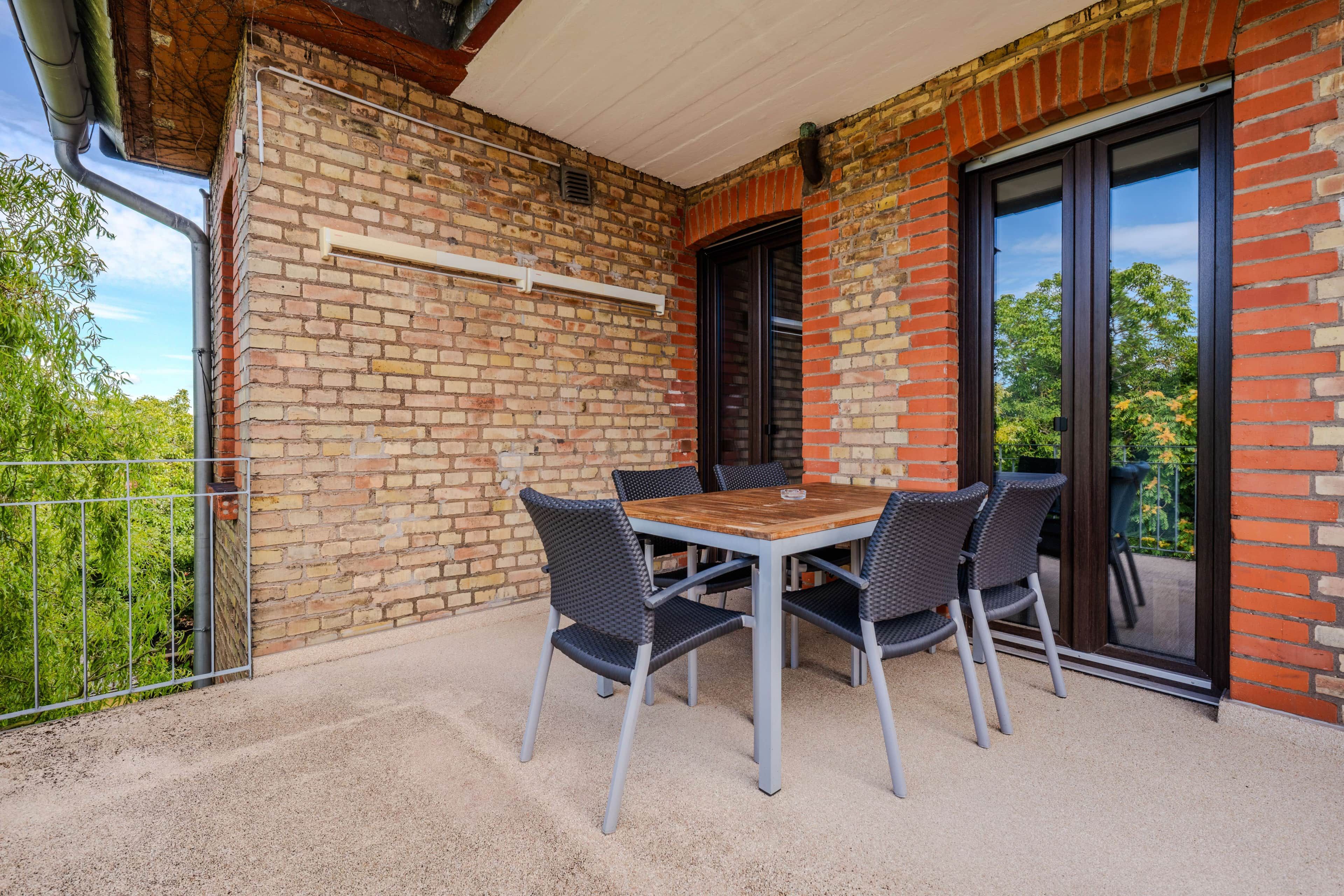 Eine Terrasse im Freien mit Tisch und Stühlen, einer Ziegelwand und einer Schiebetür.
