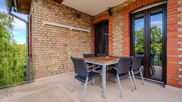 Een terras buiten met een tafel en stoelen, een bakstenen muur en een schuifpui.