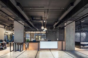 Een moderne kantoorruimte met blootgelegd ventilatiekanaal, een receptiebalie en een zithoek met tafels en stoelen.