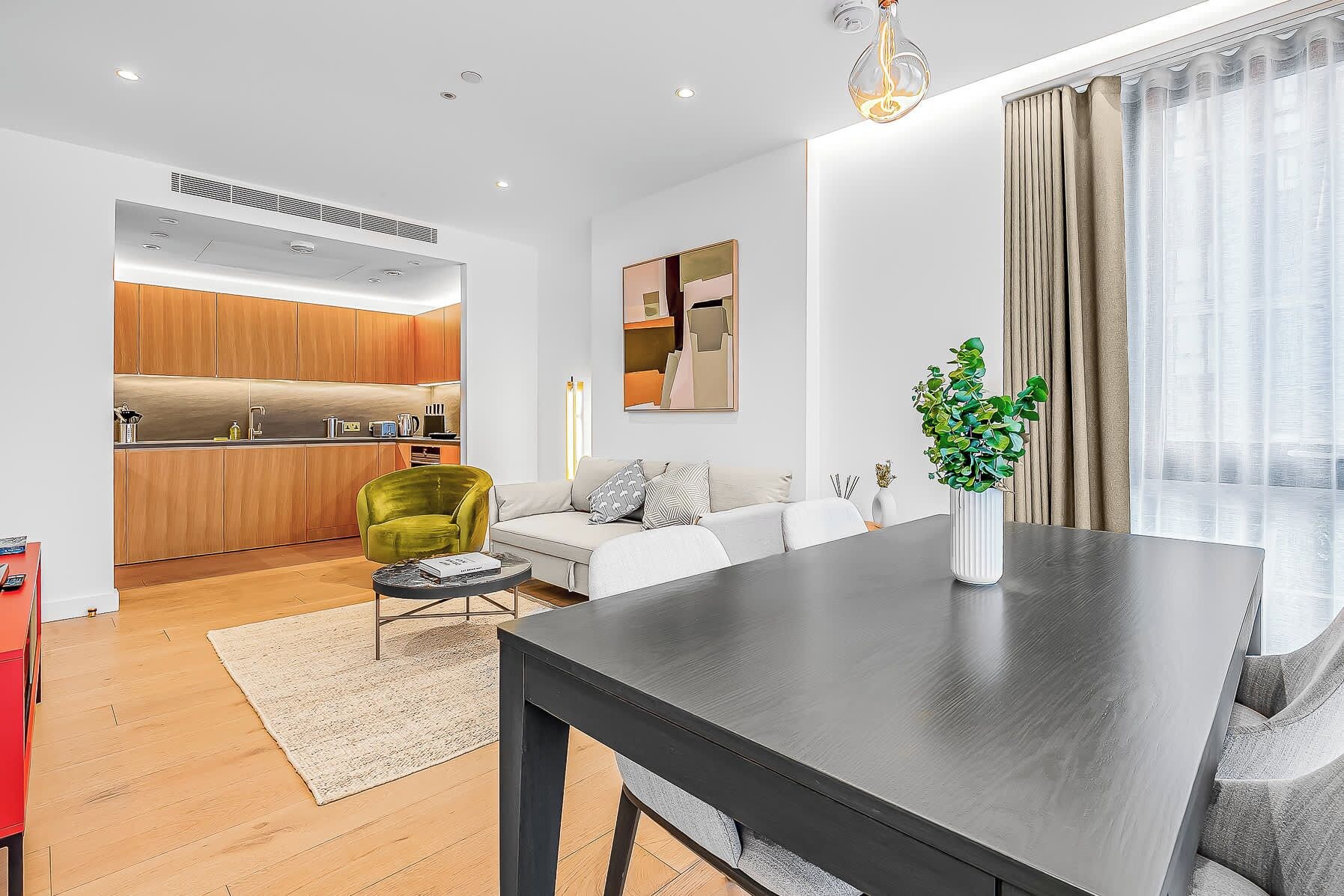 Un espace de vie moderne comprenant une table à manger, un fauteuil vert, un canapé et un coin cuisine.