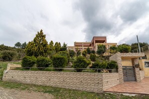 A modern building with a flat roof, surrounded by a landscaped garden with various shrubs and trees. - Apartment 'Villa Neraida - Panoramic Lake View' with Lake View, Wi-Fi and Air Conditioning (Νεράιδα)
