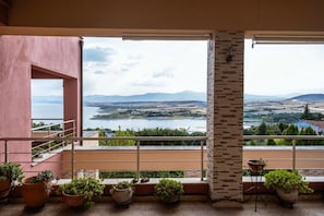 A balcony with a view of a lake and mountains, potted plants, and a stone wall.