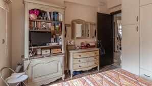 Un dormitorio con cama, tocador con espejo, televisor sobre un mueble bajo y armario.