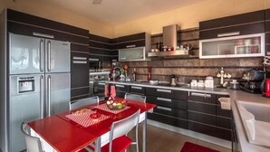 Una cocina moderna con armarios oscuros, electrodomésticos de acero inoxidable y una mesa de comedor roja.