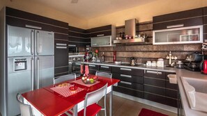 A modern kitchen with dark cabinetry, stainless steel appliances, and a red dining table. - Apartment 'Villa Neraida - Panoramic Lake View' with Lake View, Wi-Fi and Air Conditioning (Νεράιδα)
