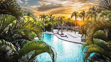 A swimming pool surrounded by palm trees and lounge chairs, with a sunset in the background.