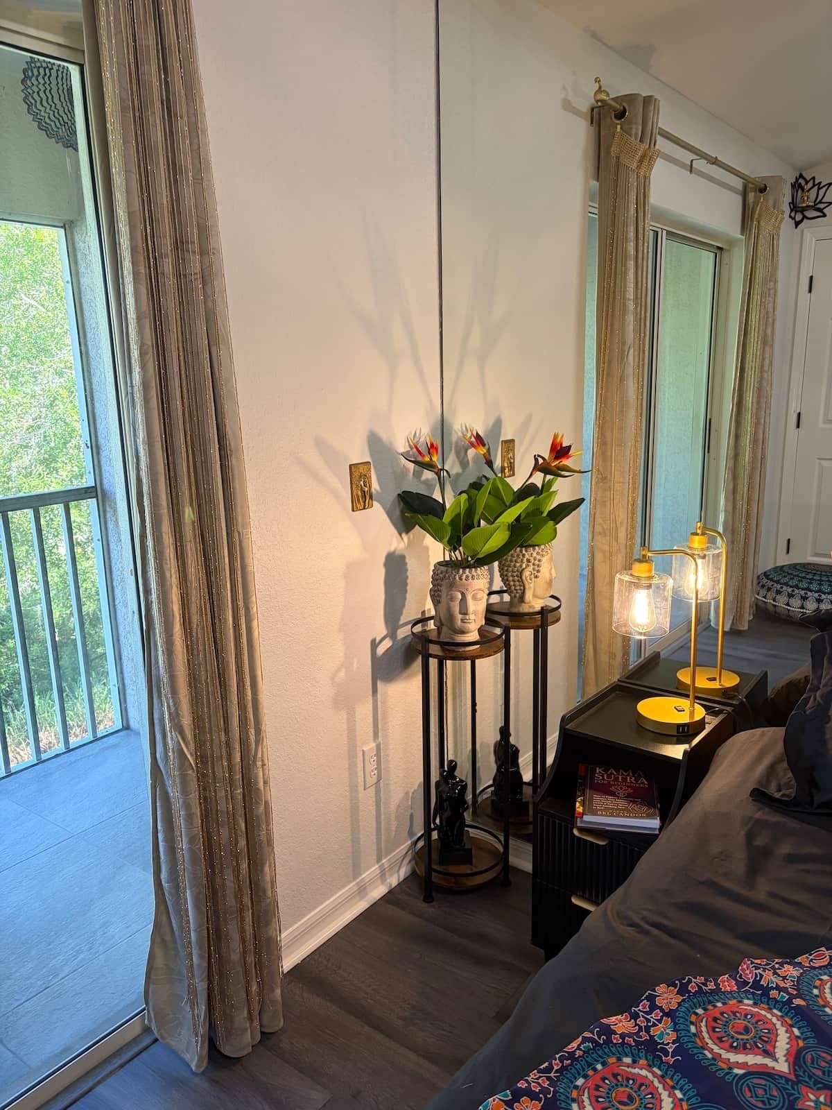 Una habitación con una cama, una mesita de noche con lámpara, una ventana con cortinas y vistas al exterior.