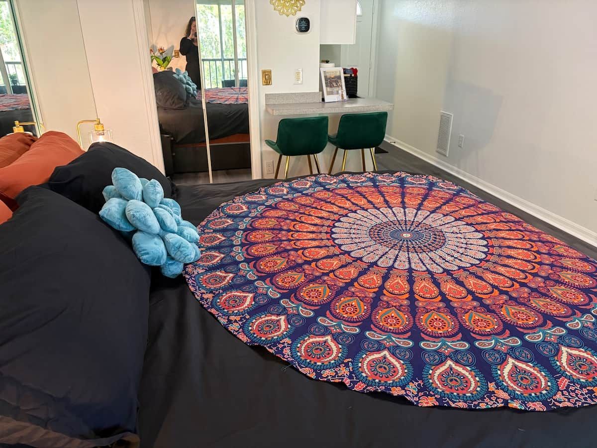 A bedroom with a large bed, a round patterned rug, and a desk with two chairs.