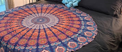 A bedroom with a large bed, a decorative tapestry, a small table with a vase of flowers, and a wall decoration.