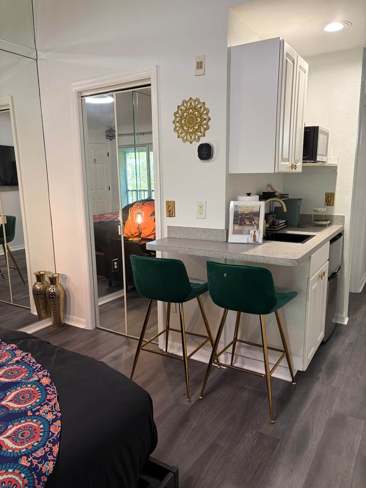 A compact kitchen with a central island, two green bar stools, and a microwave above the counter.