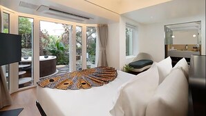 Ein modernes Hotelzimmer mit einem großen Bett, einer Sitzecke mit Blick auf den Garten und einem separaten Badezimmer mit Spiegel.