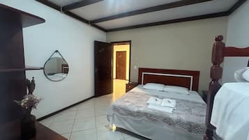 Un dormitorio con cama, mesita de noche, espejo y puerta que da a otra habitación.