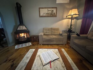 Una sala de estar acogedora con chimenea, un sofá, un tapete para leer con un libro abierto y una lámpara.