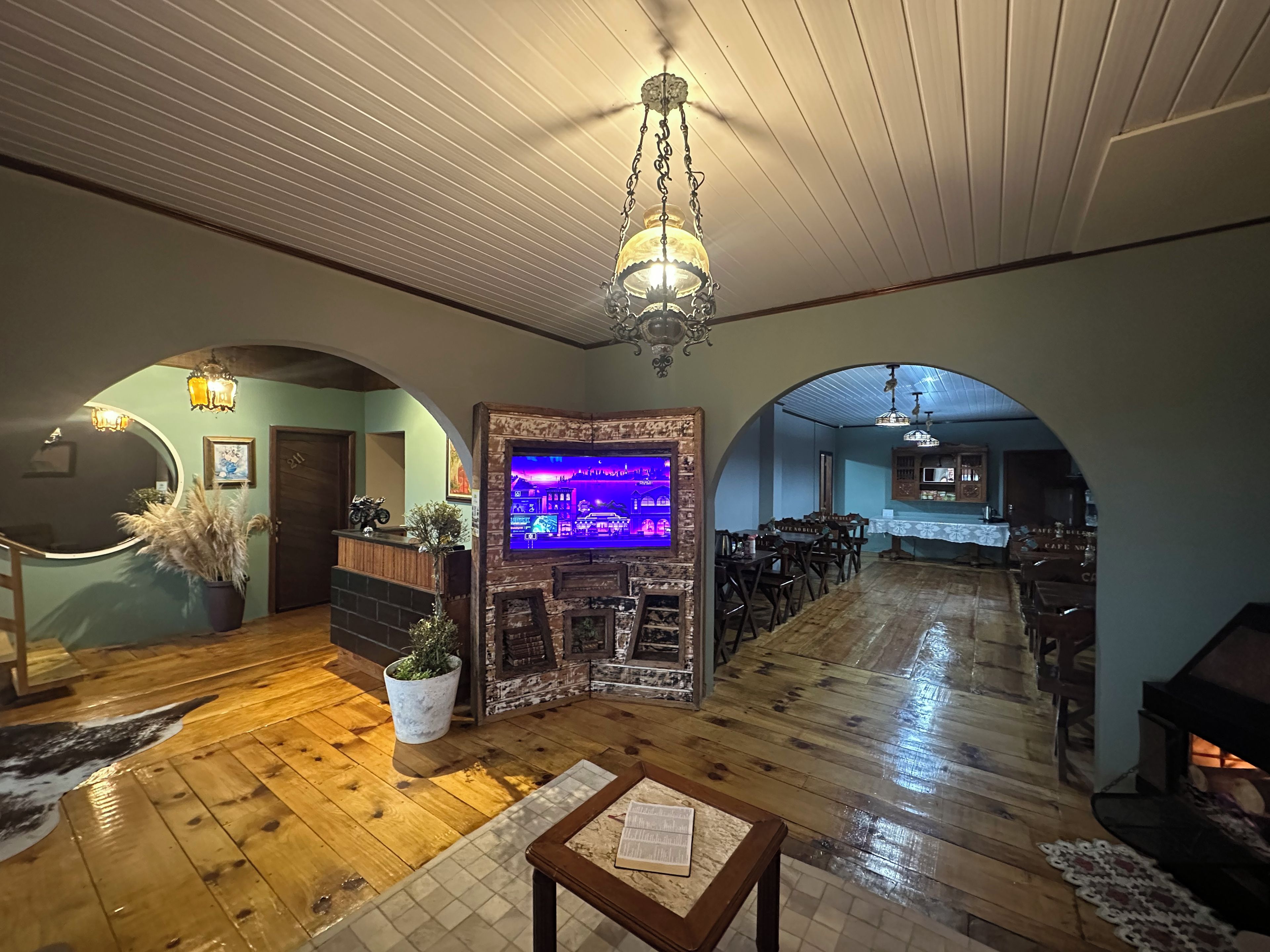 Un interior espacioso con pisos de madera, una chimenea, una zona de bar y una pantalla de televisión que muestra una escena de bar.