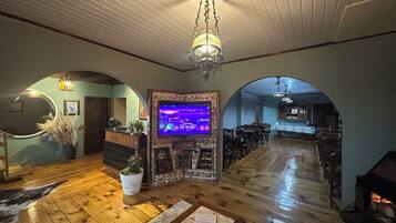 Un interior espacioso con pisos de madera, una chimenea, una zona de bar y una pantalla de televisión que muestra una escena de bar.