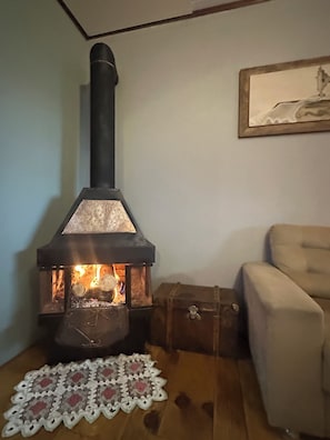 A wood-burning stove with a chimney, a cushioned armchair, and a framed picture on the wall.